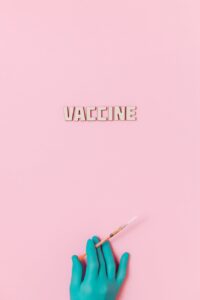vaccine text and a person wearing latex glove while holding a syringe on pink background